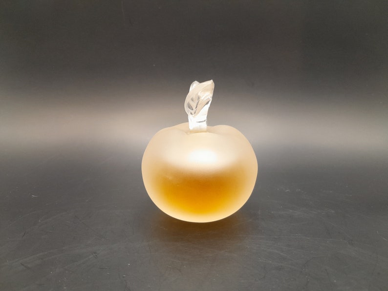 May include: A frosted glass perfume bottle shaped like an apple with a clear glass stopper. The bottle is filled with a light amber liquid.