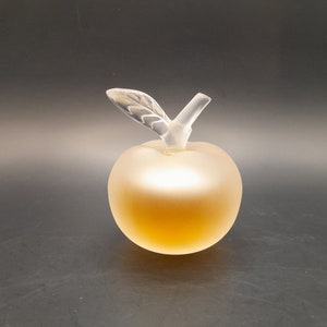 May include: A clear glass apple-shaped bottle with a frosted finish. The bottle has a clear glass stem and leaf.