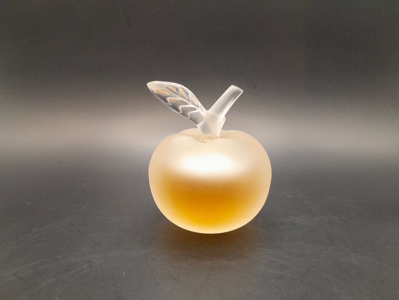 May include: A clear glass apple-shaped bottle with a frosted finish. The bottle has a clear glass stem and leaf.