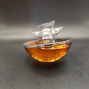 Puede incluir: Un frasco de perfume de vidrio transparente con un l&iacute;quido dorado en su interior. El frasco tiene un dise&ntilde;o &uacute;nico y en capas con una tapa plateada.