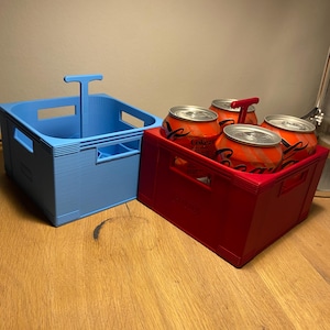Può includere: Due portabevande in plastica. Uno è azzurro e vuoto, l'altro è rosso e contiene quattro lattine di Coca-Cola. Entrambi i portabevande hanno una maniglia per un facile trasporto. I portabevande sono su una superficie di legno.