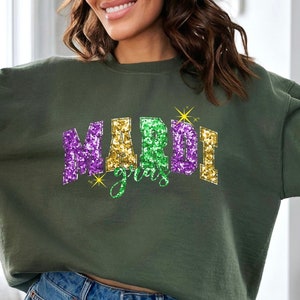 May include: A green sweatshirt with a glittery purple, gold, and green "Mardi Gras" design.