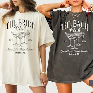 May include: Two oversized t-shirts, one cream and one charcoal, featuring the text "THE BRIDE CLUB" and "THE BACH CLUB" respectively. Each shirt has a martini glass graphic, the year "2025", and "Jennifer's Bachelorette, Miami, FL".