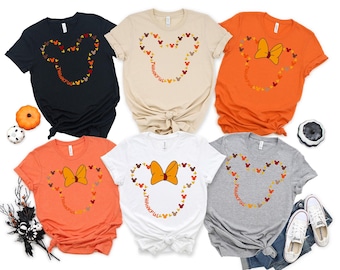 May include: A collection of six t-shirts in various colors, including black, beige, orange, white, and gray. Each shirt features a Mickey Mouse head outline made of fall-colored Mickey heads, with the word "Thankful" in the center.