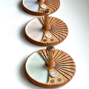 Può includere: Tre organizer da scrivania in legno dal design circolare. Ogni organizer ha un vassoio colorato chiaro, un manico in legno e un motivo a raggiera. I vassoi sono dipinti in azzurro, bianco sporco e verde menta.