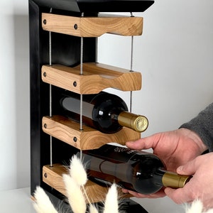 May include: A black metal wine rack with four wooden shelves, each with a curved design to hold wine bottles. The rack is suspended by metal cables and has a modern, minimalist design.