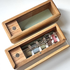 May include: Two wooden boxes with clear glass lids. The smaller box contains a set of colorful embroidery floss and a pair of small scissors. The larger box is empty.
