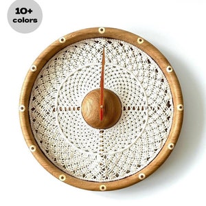 May include: A round wooden clock with a white crocheted design and gold accents. The clock has a red hour hand and a white minute hand.