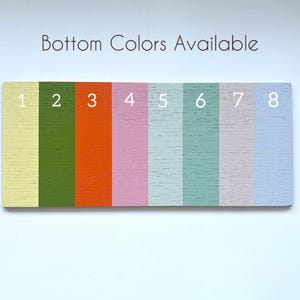 May include: A rectangular wooden sign with eight vertical stripes in various colors: yellow, green, orange, pink, light blue, and gray. The text "Bottom Colors Available" is at the top, with numbers 1-8 next to each color.