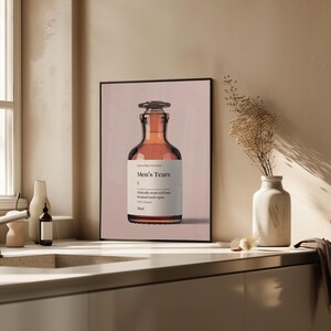 Puede incluir: Una botella de vidrio marr&oacute;n con una etiqueta que dice "Men's Tears" y "Ethically sourced from bruised male eyes". La botella est&aacute; sobre un fondo rosa.