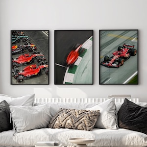 May include: Three framed prints of red Formula One race cars on a racetrack. The cars are in motion, with the first print showing three cars in a line, the second print showing a single car in a blur, and the third print showing a single car in motion.