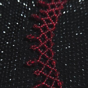 May include: Close-up of a black fabric with a red, open-weave design along the edge. The design is made of small, connected diamond shapes. The background has a subtle sparkle effect, with tiny white dots scattered across the surface.