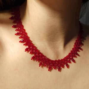 May include: A vibrant red beaded necklace. The necklace features a delicate, intricate design with small, round beads. The color is a deep, rich red, creating a striking visual effect. The necklace is designed to sit around the neck.