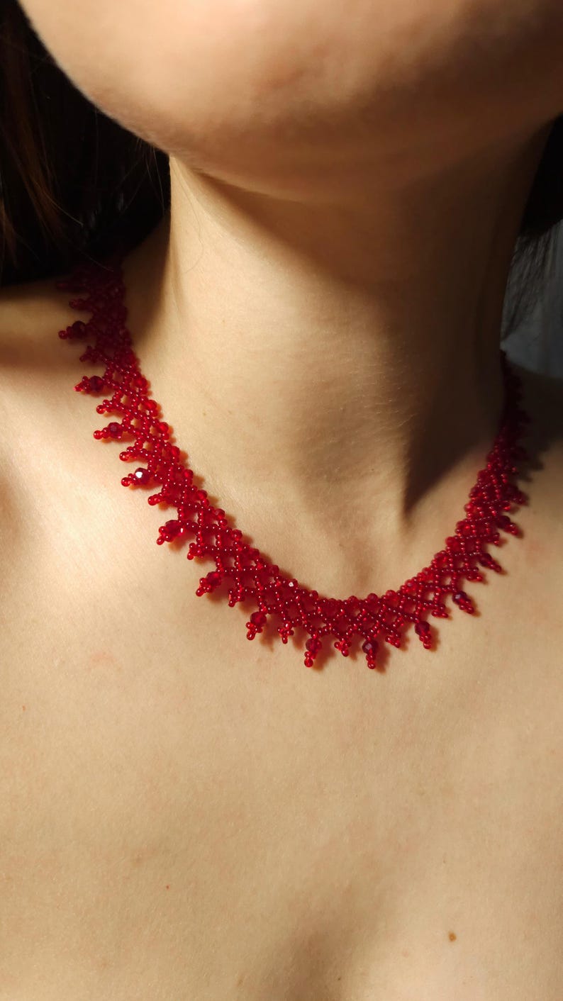 May include: A vibrant red beaded necklace. The necklace features a delicate, intricate design with small, round beads. The color is a deep, rich red, creating a striking visual effect. The necklace is designed to sit around the neck.