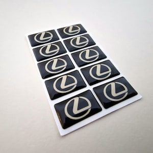 May include: A sheet of 12 black and silver Lexus car logo stickers. The stickers are arranged in four rows of three.