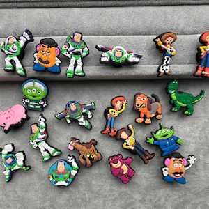 May include: A selection of colourful character shoe charms featuring designs from the animated movie series. The charms include characters like Buzz Lightyear, Woody, and others, in various poses and colours.