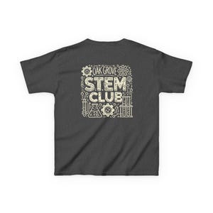 Puede incluir: Camiseta gris oscuro con un diseño gráfico blanco que dice "Oak Grove STEM Club" con ilustraciones de engranajes, vasos de precipitados y tubos de ensayo.