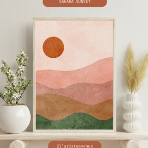 Könnte beinhalten: Abstrakter Kunstdruck mit einem Sonnenuntergang über einer Wüstenlandschaft. Der Druck zeigt eine große orange Sonne, rosa und braune Hügel und grüne Täler. Der Druck ist gerahmt und enthält den Text "SAHARA SUNSET" und "@l'aristeavenue".