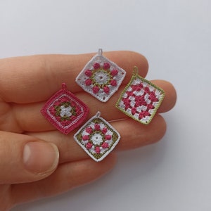 Könnte beinhalten: Vier gehäkelte Quadrate in Rosa, Weiß und Grün. Jedes Quadrat hat ein anderes Muster in der Mitte.