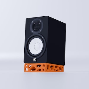 Op de afbeelding: Zwarte studiomonitorluidspreker op een oranje luidsprekerstandaard. De luidspreker heeft een witte woofer en een kleinere zwarte tweeter.
