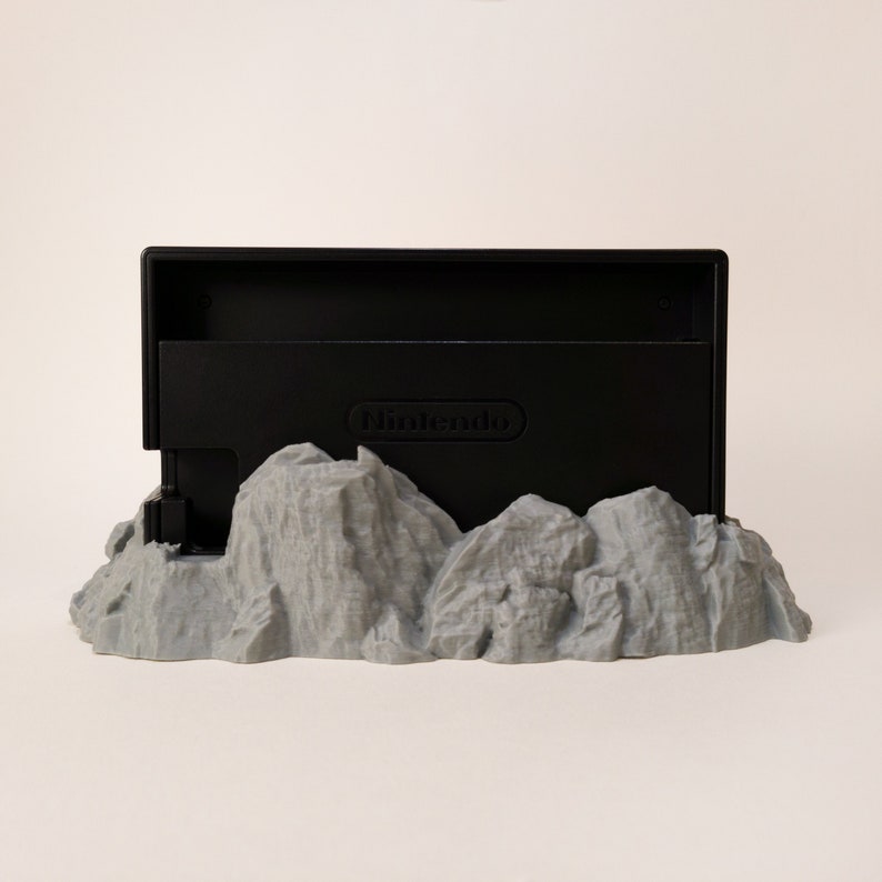 May include: A black Nintendo Switch game cartridge holder with the Nintendo logo on the front, sitting on a grey 3D printed mountain base.
