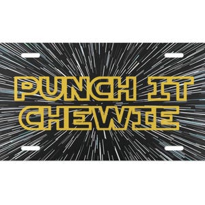 Könnte beinhalten: Rechteckiges Nummernschild mit dem Text "PUNCH IT CHEWIE" in Gelb auf schwarzem Hintergrund mit weißen Geschwindigkeitslinien. Die Platte hat vier Befestigungslöcher.