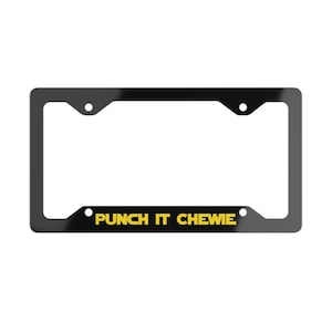May include: A rectangular black license plate frame featuring the yellow text PUNCH IT CHEWIE printed along the bottom edge. The frame includes four circular mounting holes, two at the top and two at the bottom, designed for standard vehicle attachment.