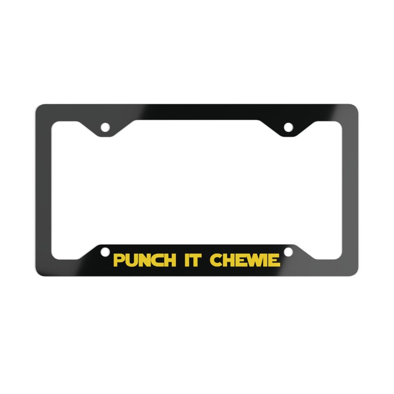 May include: A rectangular black license plate frame featuring the yellow text PUNCH IT CHEWIE printed along the bottom edge. The frame includes four circular mounting holes, two at the top and two at the bottom, designed for standard vehicle attachment.