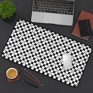 May include: Black and white checkered mouse pad with a white Mickey Mouse head pattern. The mouse pad is on a black surface with a laptop, a notebook, a cup of coffee, and pencils.