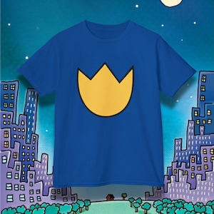 Puede incluir: Camiseta azul real con un gran diseño de tulipán amarillo. La camiseta está colocada sobre un fondo de paisaje urbano bajo un cielo nocturno. El diseño es simple y audaz, ideal para el uso diario.
