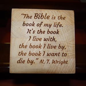May include: A wooden block with the quote "The Bible is the book of my life. It's the book I live with, the book I live by, the book I want to die by." by N.T. Wright, engraved in a brown font.