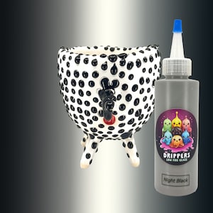 Könnte beinhalten: Ein schwarz-weißer Keramiktopf mit einem Tupfenmuster und vier Beinen. Der Topf ist mit einer schwarzen Glasur gefüllt und hat eine rote Lippe. Die Glasur ist mit "Drippers Low Fire Glaze Night Black" gekennzeichnet.