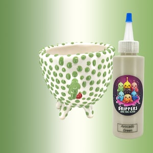 Puede incluir: Una maceta de cerámica verde con lunares blancos y tres patas. La maceta está al lado de una botella de esmalte verde aguacate de baja temperatura.