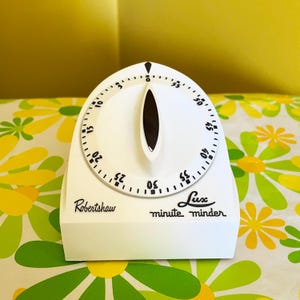 May include: A white Robertshaw Lux minute minder kitchen timer with a circular dial featuring black numbers from 0 to 55. The device has a central black indicator pointer and black text printed on the front base reading Robertshaw Lux minute minder.