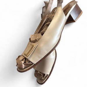 Puede incluir: Sandalias slingback de cuero beige con hebilla cuadrada dorada y tacón bajo de madera. Las sandalias están rellenas de papel marrón. Zapatos con un diseño clásico y minimalista. El tacón mide unos 5 cm.