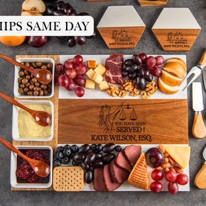 May include: A rectangular wooden and white serving board engraved with the text YOU HAVE BEEN SERVED! KATE WILSON, ESQ. and a scales of justice icon, accompanied by three white bowls with wooden spoons, cheese, fruit, crackers, and metal cheese knives.
