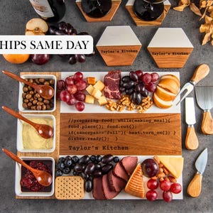 May include: A rectangular wooden and white serving board with three square bowls, wooden spoons, and cheese knives. The board features engraved code and the text Taylor's Kitchen. Includes two wine glasses and hexagonal coasters.