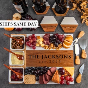 May include: A wooden serving board with a marble insert, featuring a variety of cheeses, meats, fruits, and nuts. The board is personalized with the text "THE JACKSONS est. 2023".