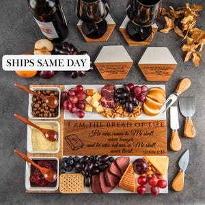May include: A white serving board with a wooden frame and a variety of snacks, including grapes, cheese, crackers, and meat. The board has a wooden plaque with the text "I AM THE BREAD OF LIFE. He who comes to Me shall never hunger, and he who believes in Me shall never thirst. JOHN 6:35".