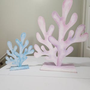 May include: Two decorative paper sea coral pieces, one blue and one pink, on a white surface. The coral is made of paper and has a watercolor effect.