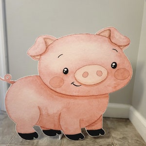 May include: A pink pig cutout with a smiling face, black eyes, and a curly tail. The pig is standing on a white base.