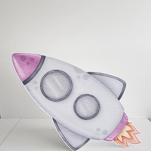 May include: A gray and white rocket with pink accents and a flame coming out of the back. The rocket has two round windows and a pointed nose.