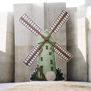 May include: A decorative windmill cutout with a green roof and body, brown blades, and small windows. A ladder leads to the top, and a circular emblem with the initials "LN" is at the base. The windmill is set against a neutral background.