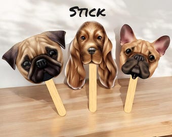 May include: Three pet face cutouts on wooden sticks featuring a pug, a spaniel, and a French bulldog. The text PET FACE ON A STICK is printed above the dog heads. Each cutout displays a realistic, detailed color illustration of a dog's face.