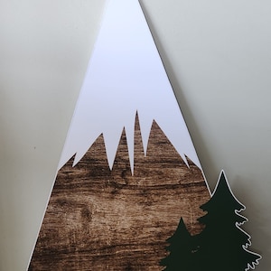 May include: A large wooden mountain cutout with a white snow-capped peak and a dark brown, wood-grain textured base. A green tree silhouette is on the right side. The mountain is approximately 4 feet tall.