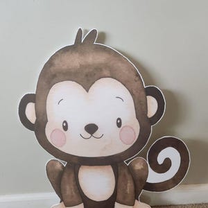 May include: A brown and white cartoon monkey cutout with a curled tail. The monkey has a friendly face with pink cheeks and a small, white nose.