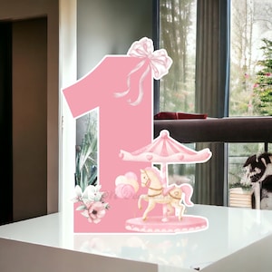 May include: Pink number one with a carousel horse and a pink bow. The number one is decorated with white flowers and pink balloons.