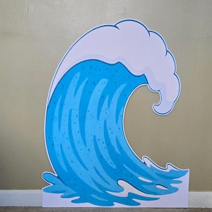 May include: A flat, die-cut cardboard cutout featuring a stylized illustration of a large ocean wave. The wave is depicted in shades of bright blue and light blue with a white crest at the top and white foam details at the base, outlined in blue.