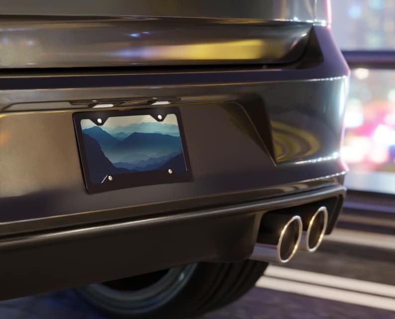 K&ouml;nnte beinhalten: Schwarzer Kennzeichenrahmen mit einem Berglandschaftsdesign. Das Kennzeichen zeigt ein blau-wei&szlig;es Gradientenbild von Bergketten. Der Rahmen ist an der R&uuml;ckseite eines dunkelgrauen Fahrzeugs angebracht.