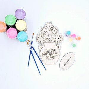 May include: A wooden craft kit for painting a vase with flowers. The kit includes a wooden vase with the text "Happy Mother's Day!" and six wooden flowers. The kit also includes six bottles of paint, three paintbrushes, and a wooden stand.